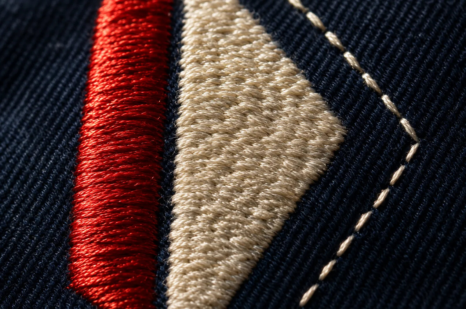 Macro de un bordado con puntada de satín, relleno y pespunte en hilos rojo, crema y azul marino