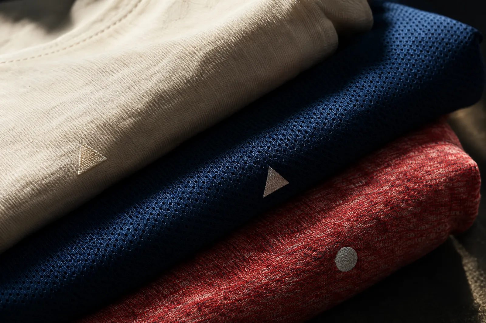 Tres playeras dobladas de algodón, poliéster dry-fit y mezcla, con la textura de cada tela