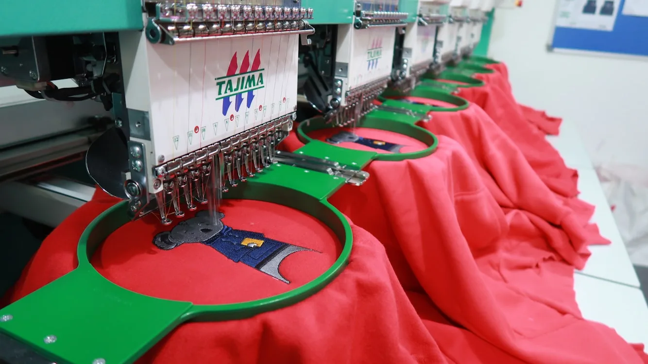 Fila de cabezales de bordado Tajima trabajando a la vez sobre prendas rojas montadas en bastidores