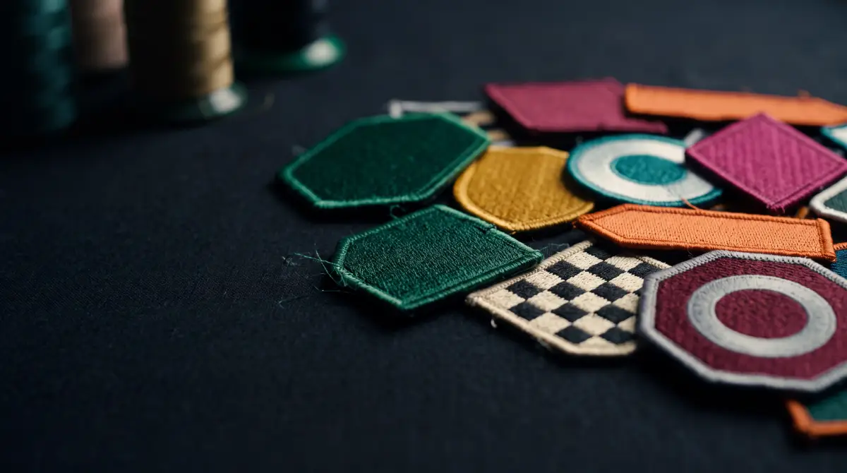 Parches bordados de distintas formas y colores: hexágonos verdes, círculos mostaza, rombos magenta y una escarapela turquesa